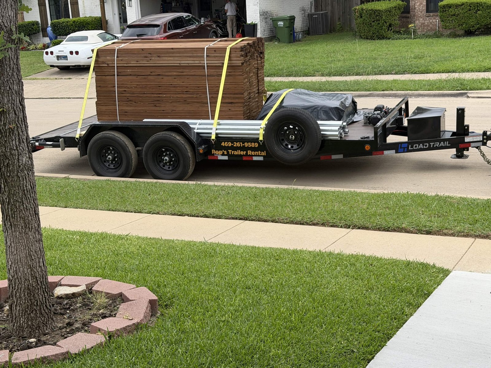 Pop's Trailer Rental car hauler loaded with lumber and metal pipe, yellow straps