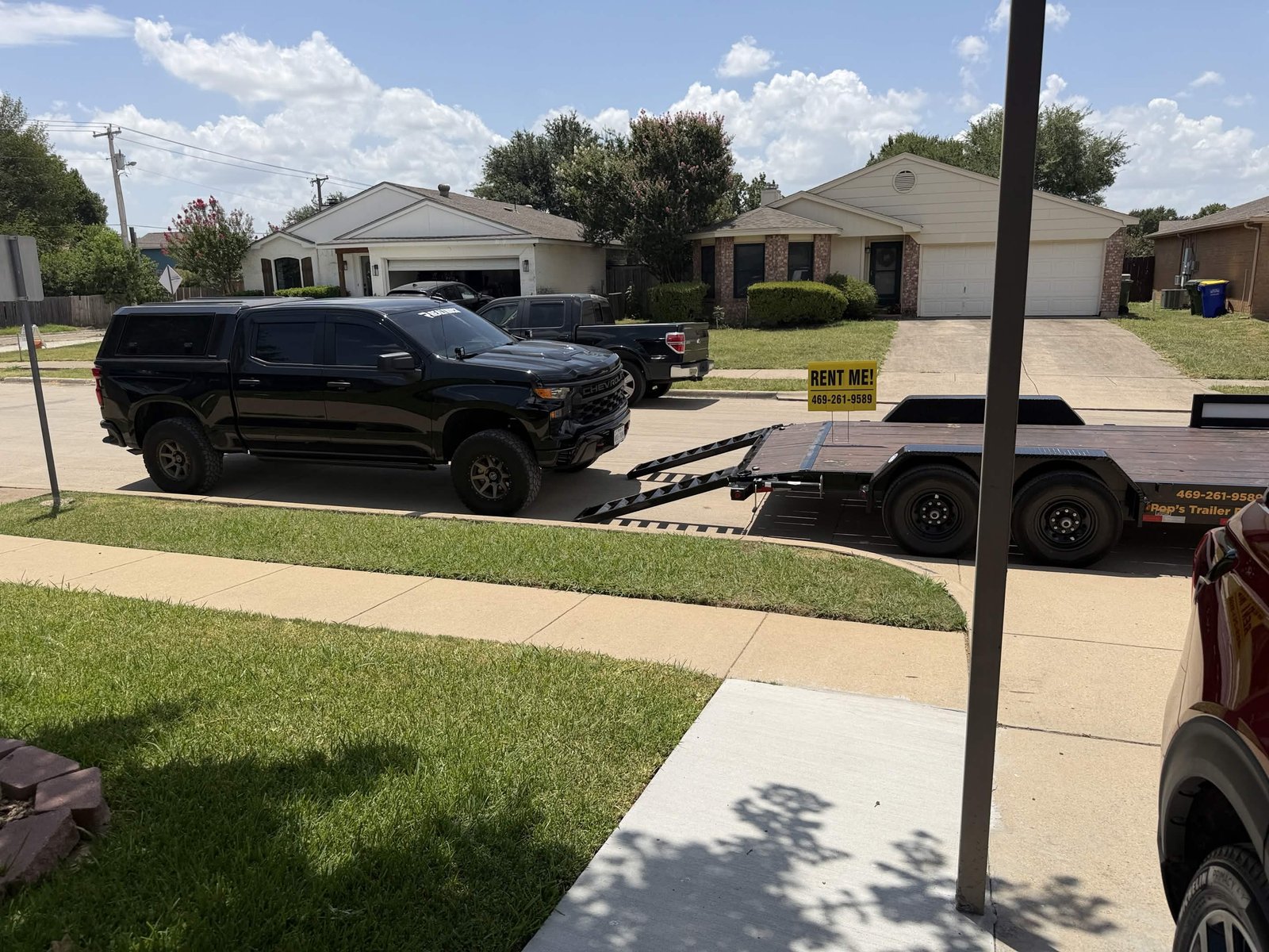 Black car hauler with ramps down and yellow RENT ME sign next to a truck